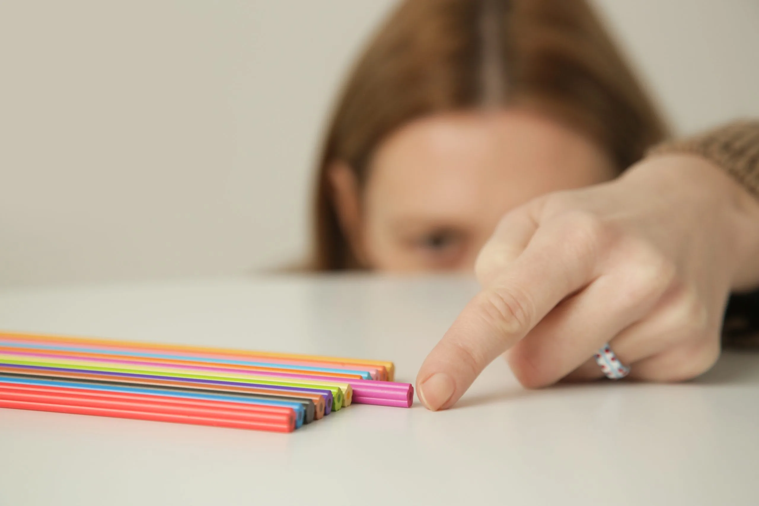 Child's hand selecting a pink colored pencil from a row of multicolored pencils
