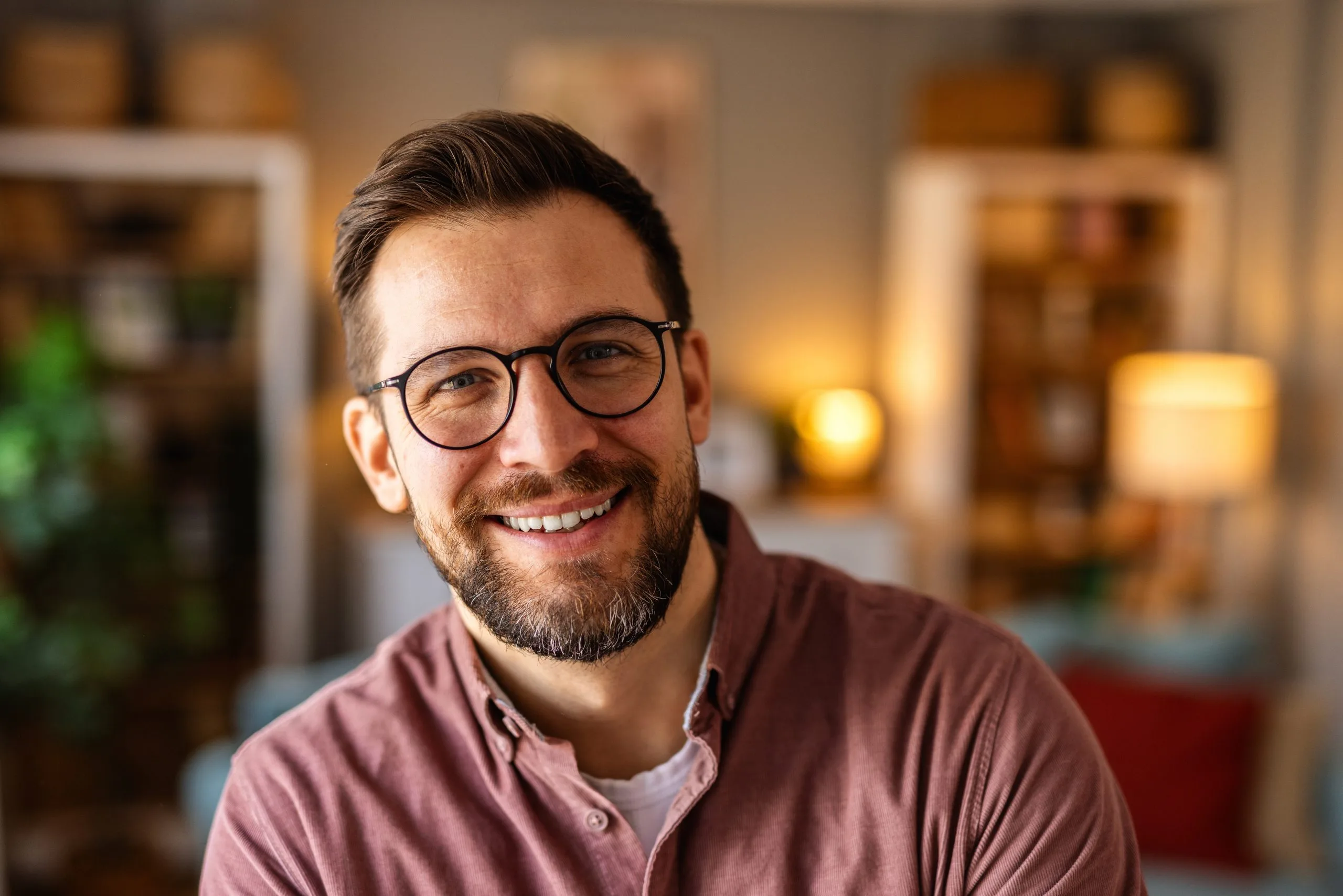 Man with glasses and beard smiling in a warm, professionally lit office setting