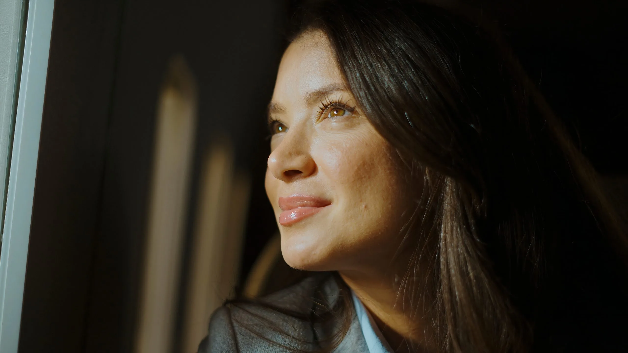 Woman in dark clothing looking thoughtfully to the side near window with warm lighting