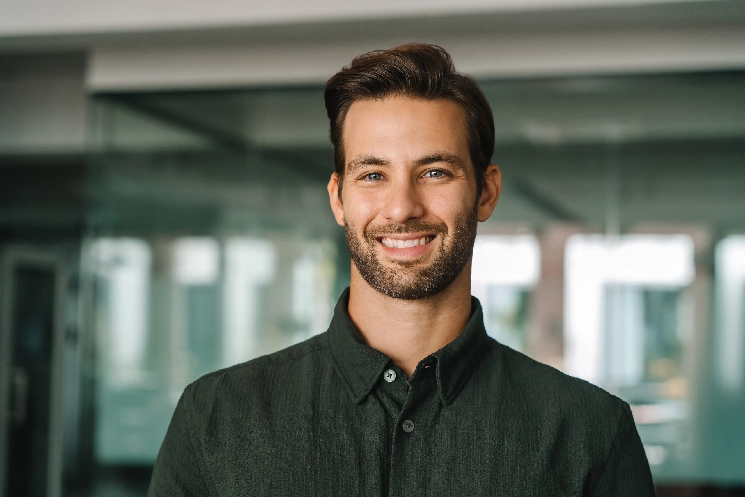 Man in dark button-up shirt smiling in modern office with glass partitions