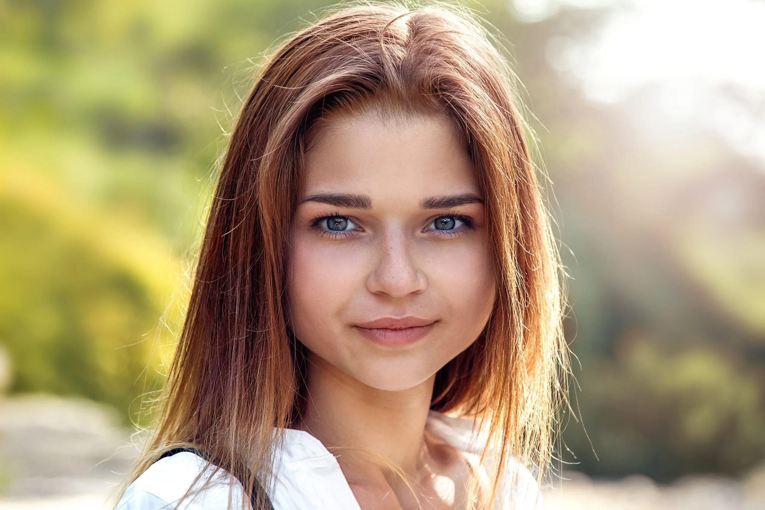 Woman with reddish-brown hair in white shirt looking at camera with green background