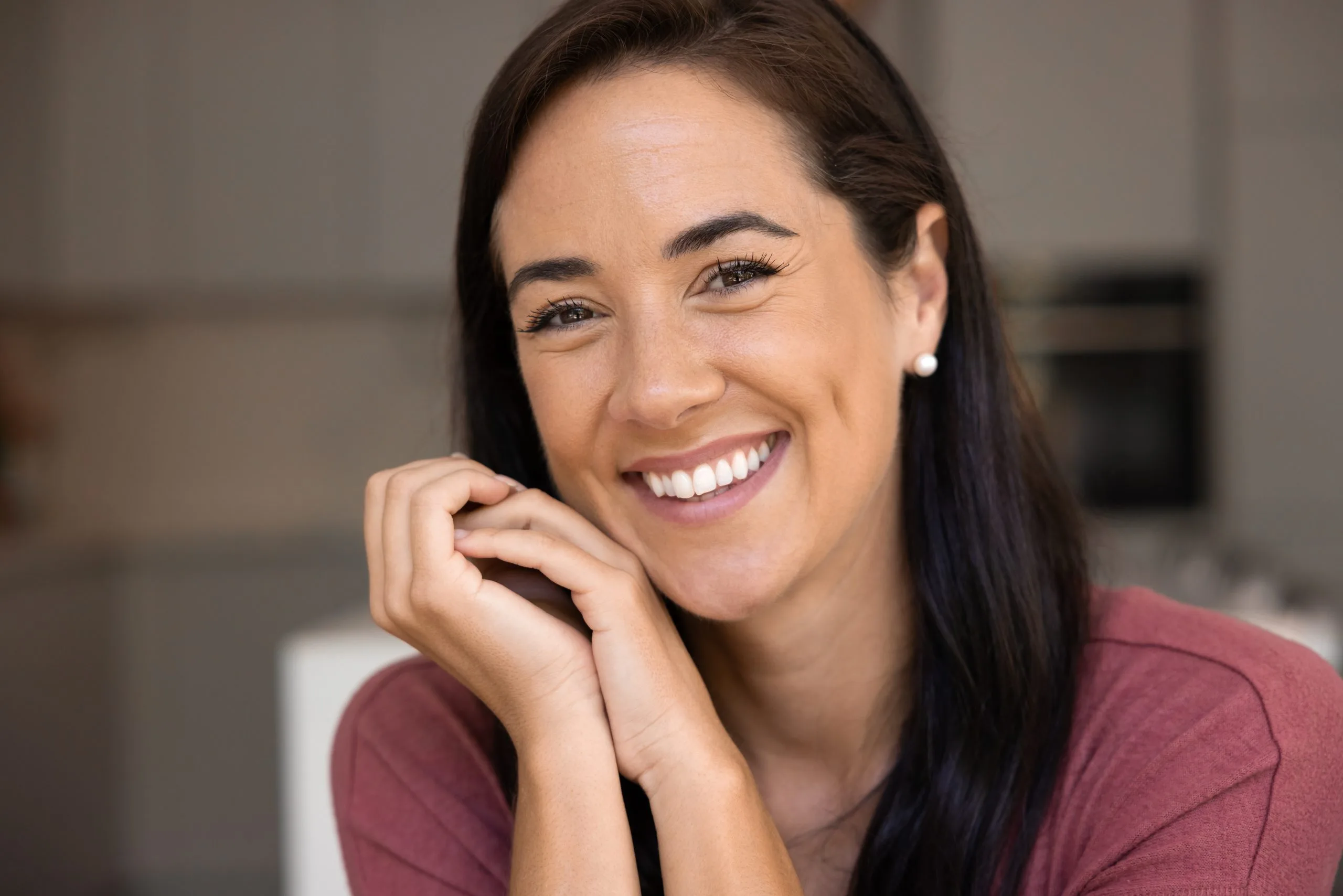 Woman in burgundy shirt smiling with hand near face in modern interior