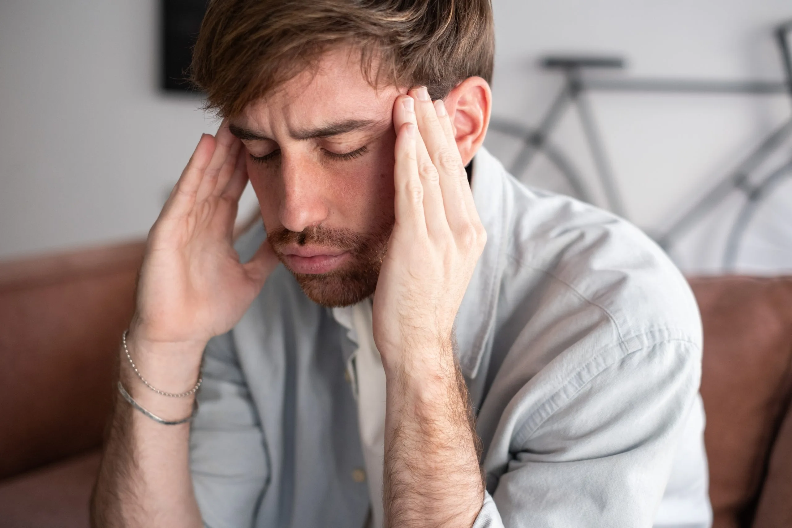 Man in light blue shirt holding his head with both hands, eyes closed, expressing stress or pain