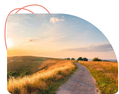 Dirt path winding through golden grassland at sunset with rolling hills