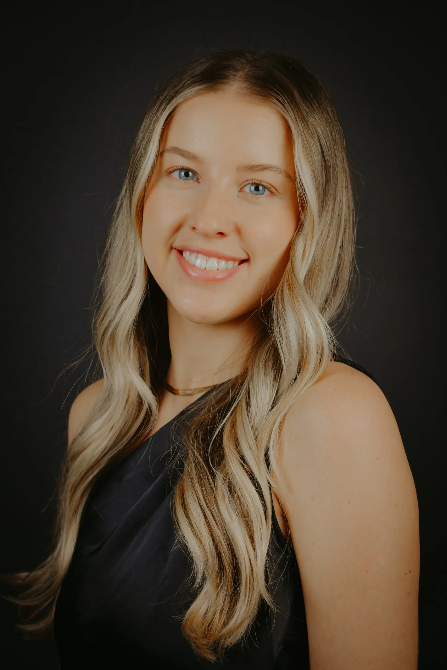 Woman with long blonde hair smiling at camera against dark background