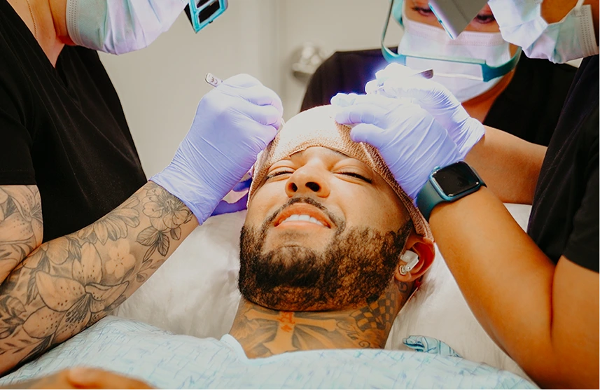 Two clinicians in purple gloves performing hair treatment on male patient lying down