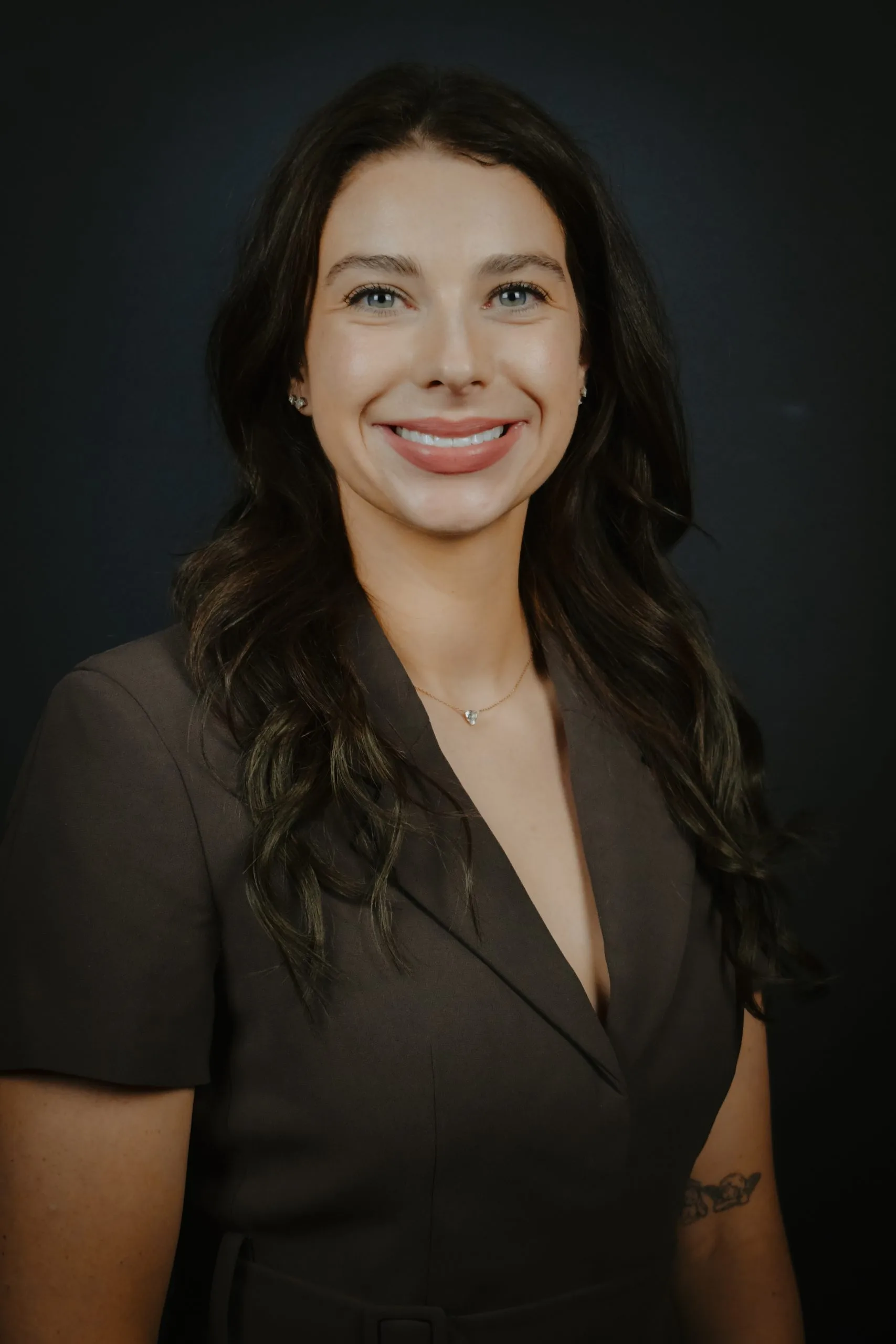 Professional headshot of woman with long dark hair smiling against dark background