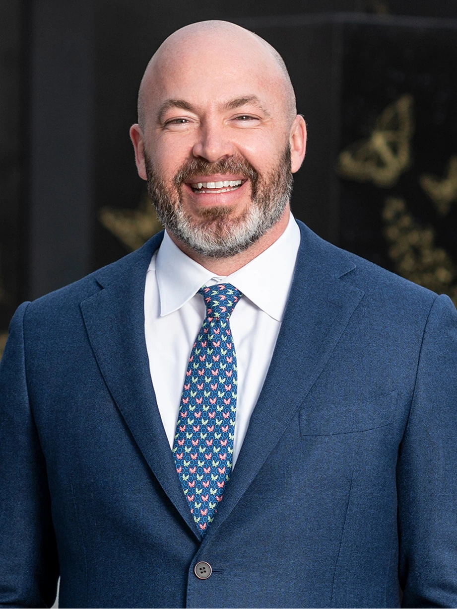 Professional headshot of man in navy blazer and patterned tie, smiling