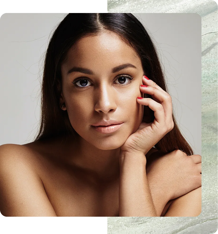 Woman with clear, glowing skin touching her face against neutral background