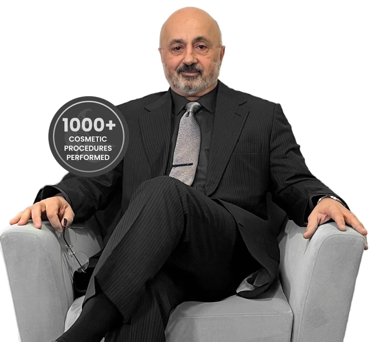 Man in dark pinstriped suit and tie seated in gray chair with badge stating 1000+ Cosmetic Procedures Performed
