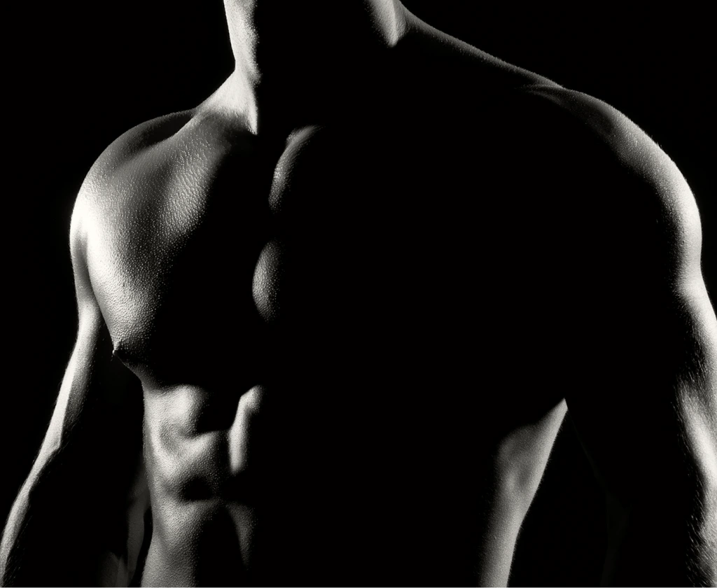 Shirtless man displaying defined abdominal and chest muscles against dark background