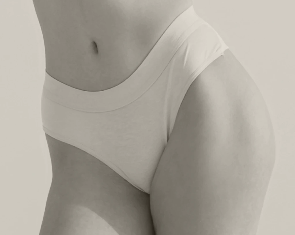 Woman's torso and hips wearing white low-rise underwear against neutral background