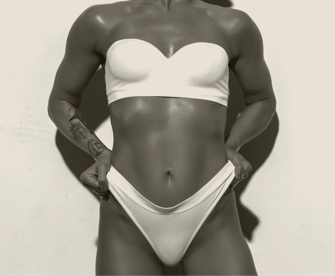 Woman in white bandeau top and briefs with hands on hips, grayscale