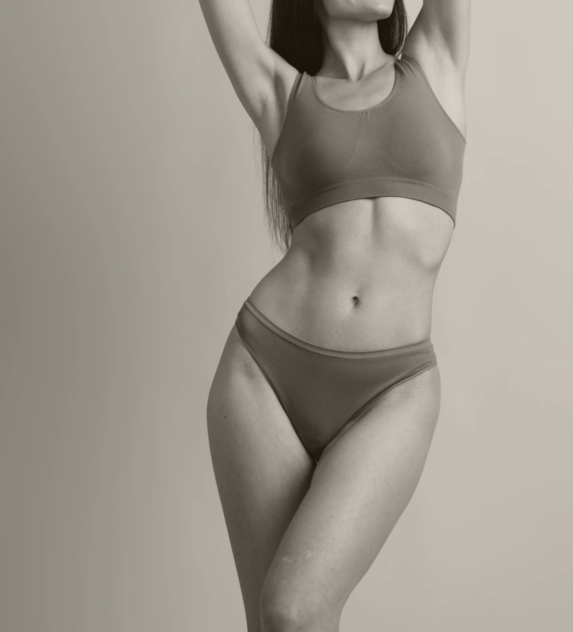 Woman in gray bra and underwear with hands behind head, displaying toned core and physique