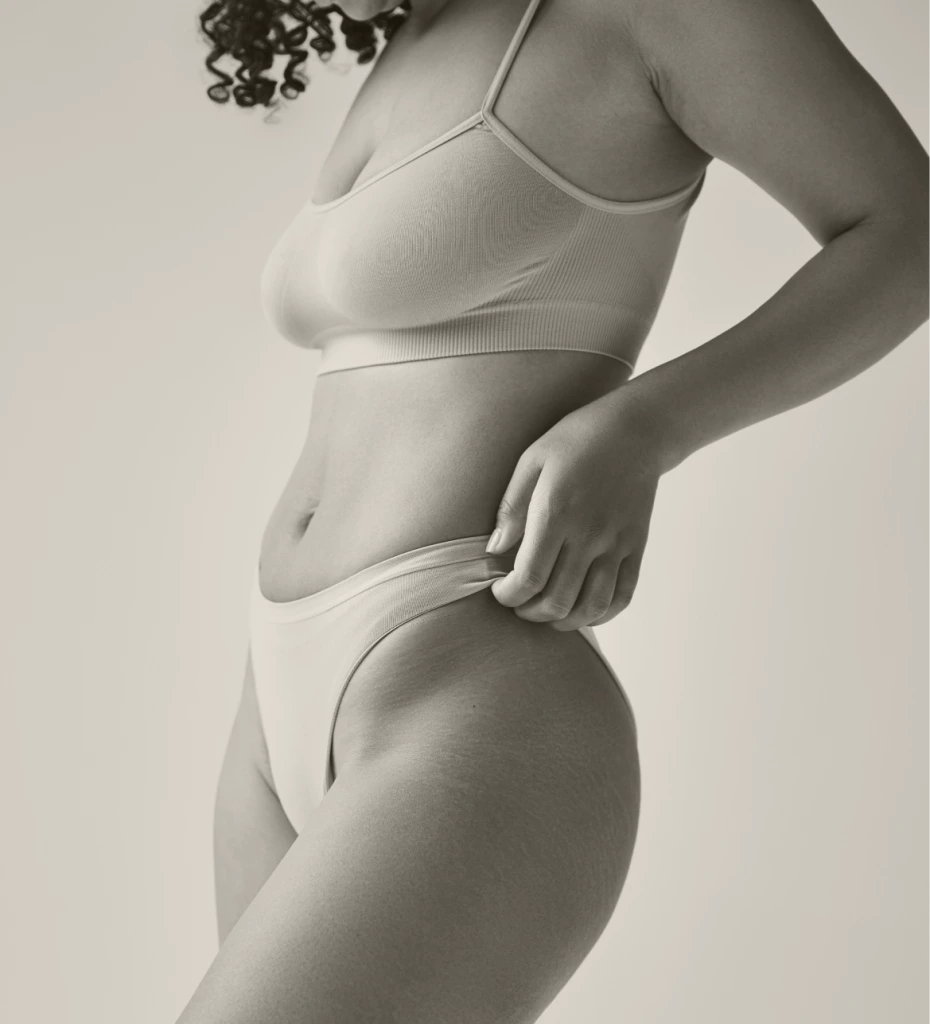 Woman in white bra and underwear with hand on hip, showing defined waist and torso