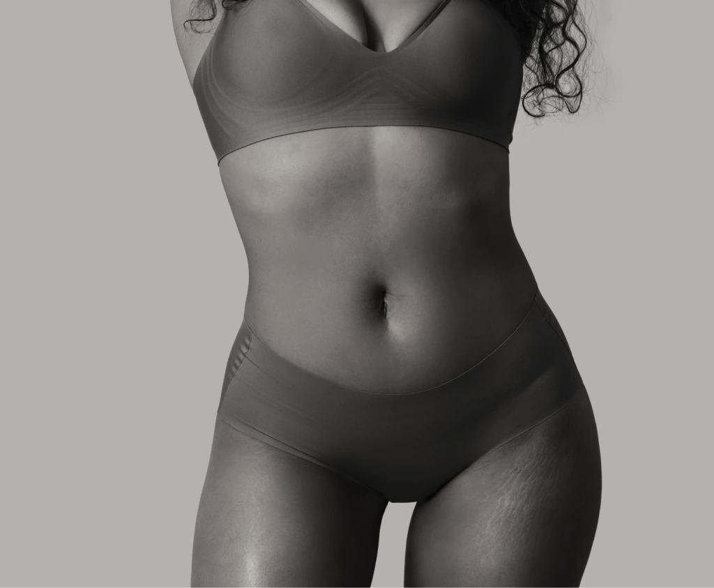 Woman in sports bra and underwear showing toned midsection against neutral background