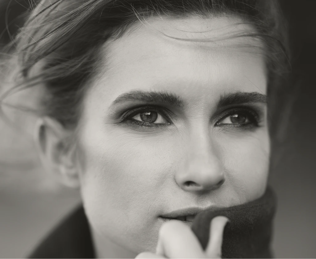 Woman with defined eyebrows and finger near lips in thoughtful expression, black and white headshot