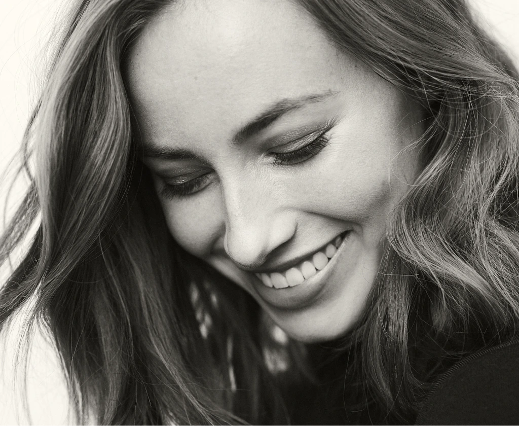 Woman with long wavy hair smiling downward in black and white portrait