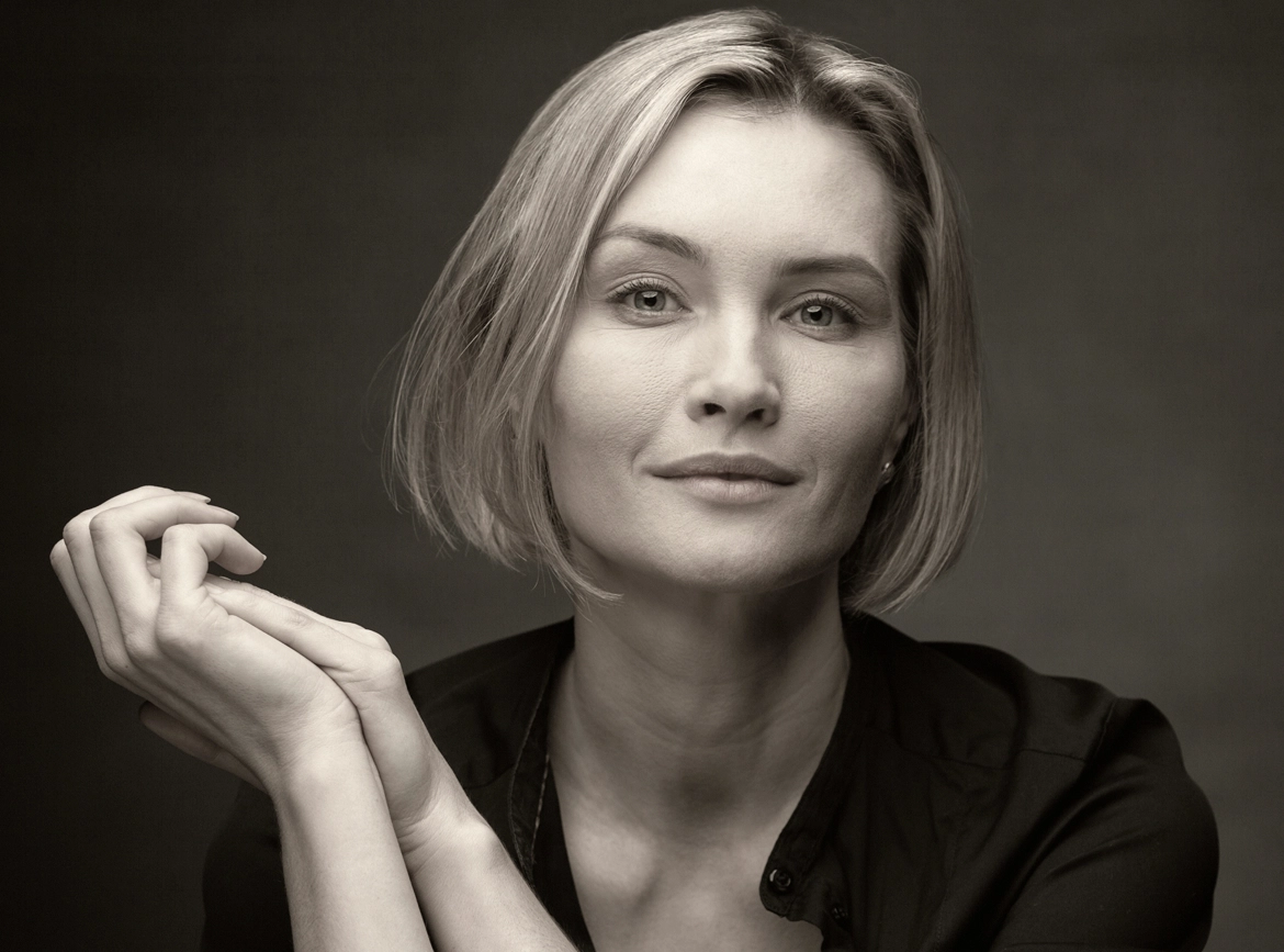 Woman with short blonde hair touching her face, shown in profile against dark background