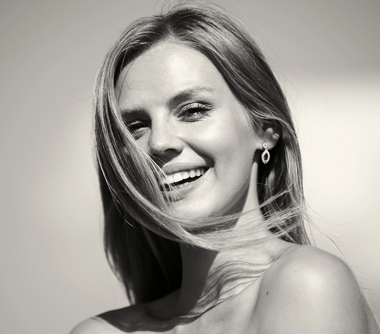 Woman with long blonde hair smiling, shown in three-quarter view against light background