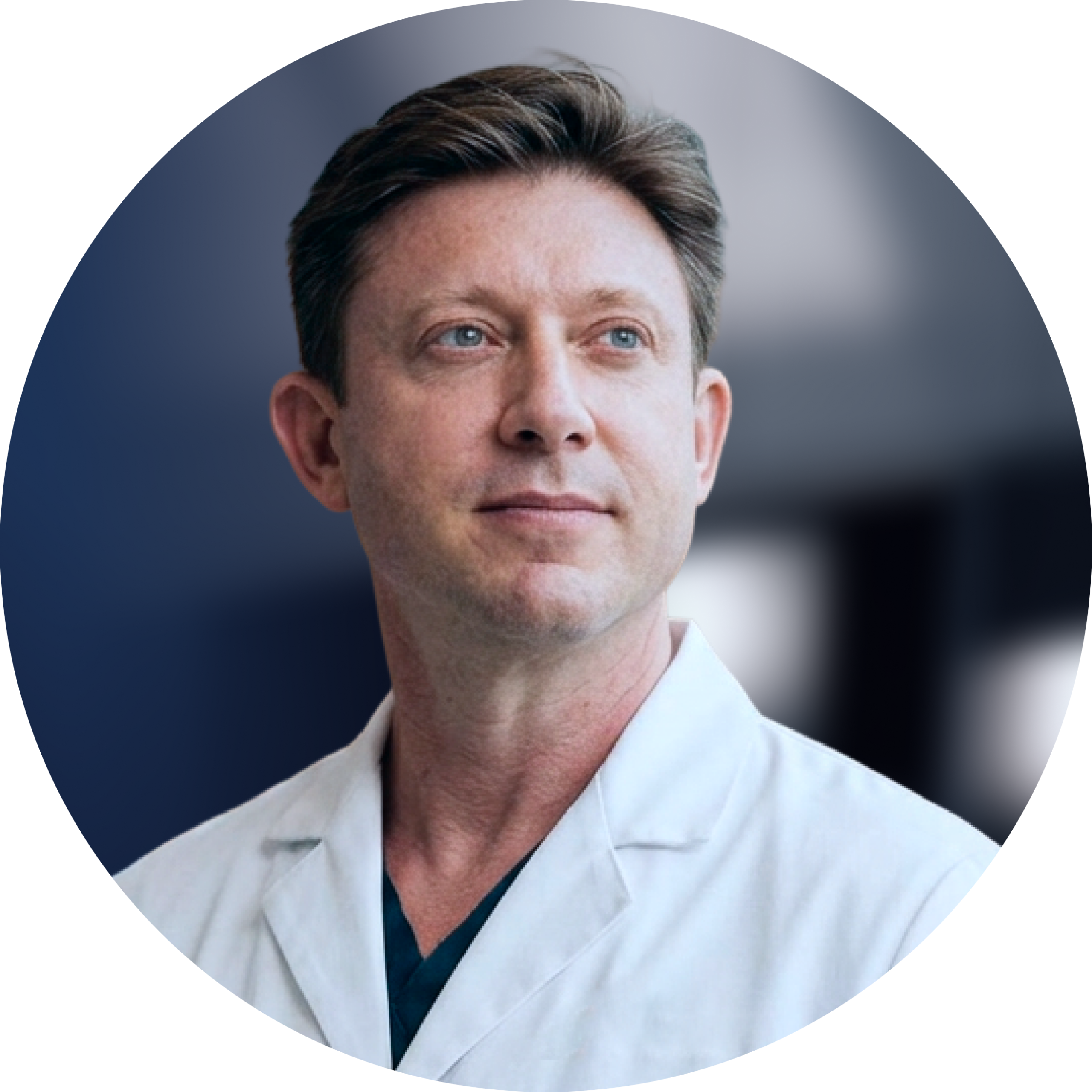 Male healthcare professional in white coat and dark scrubs against blurred clinical background