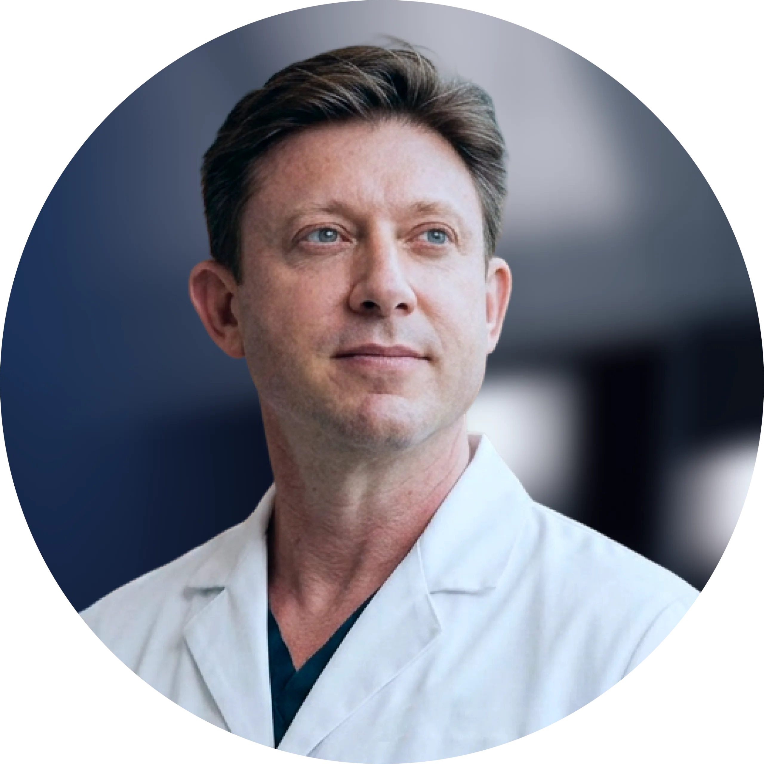 Male healthcare professional in white coat and dark scrubs against blurred clinical background
