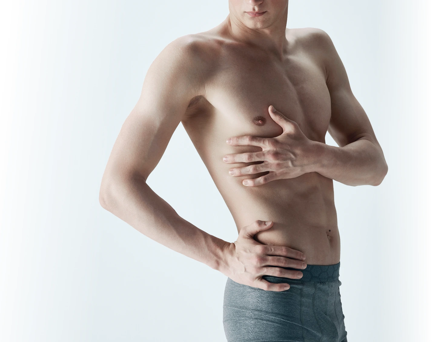 Shirtless man examining his chest and abdominal area with both hands against light background