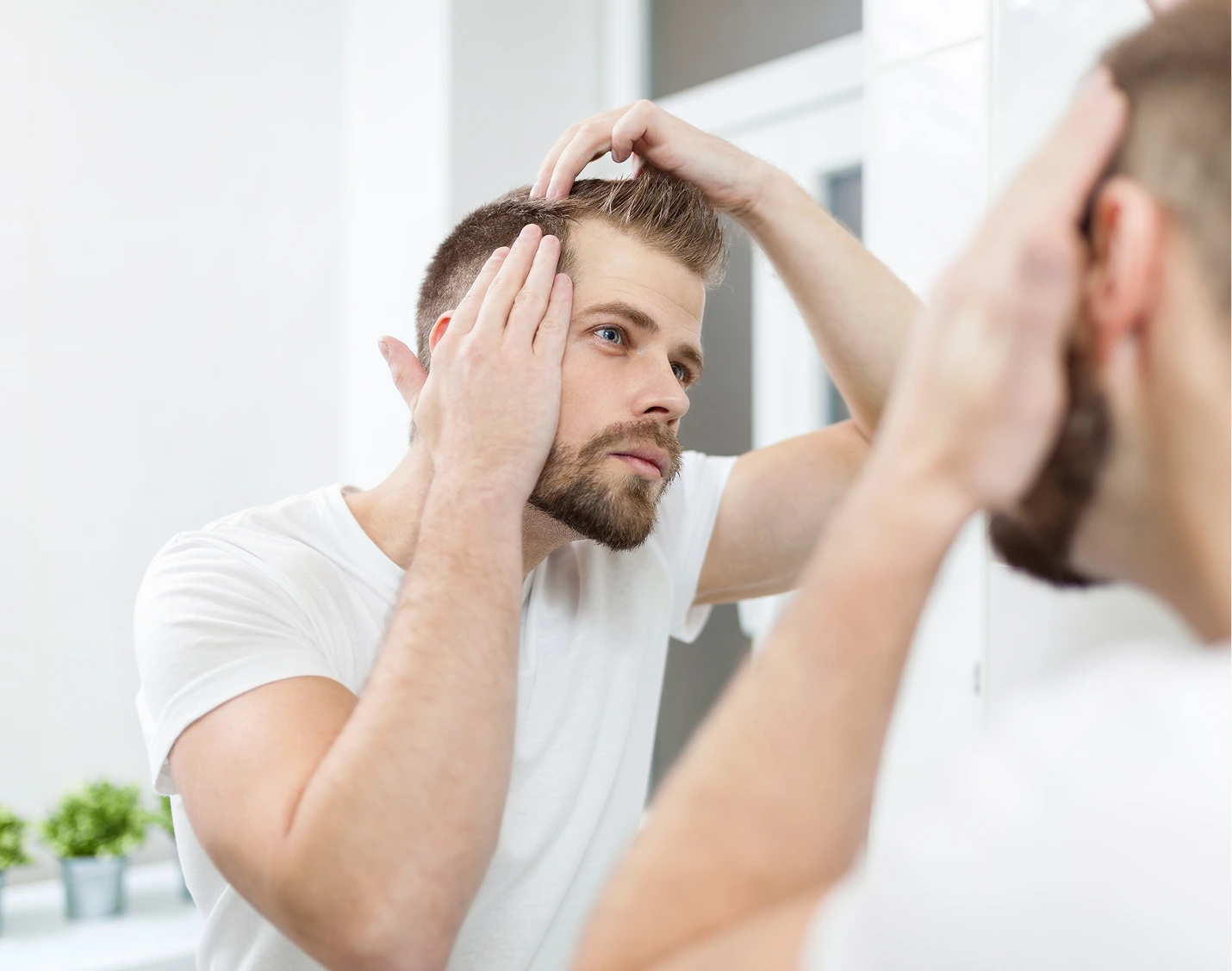 Man looking in mirror and touching his hair at the temple