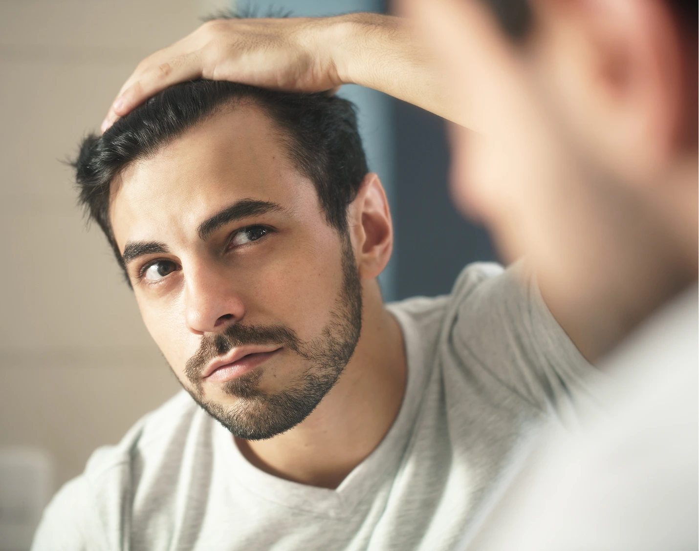 Man checking his hairline in mirror with hand on head