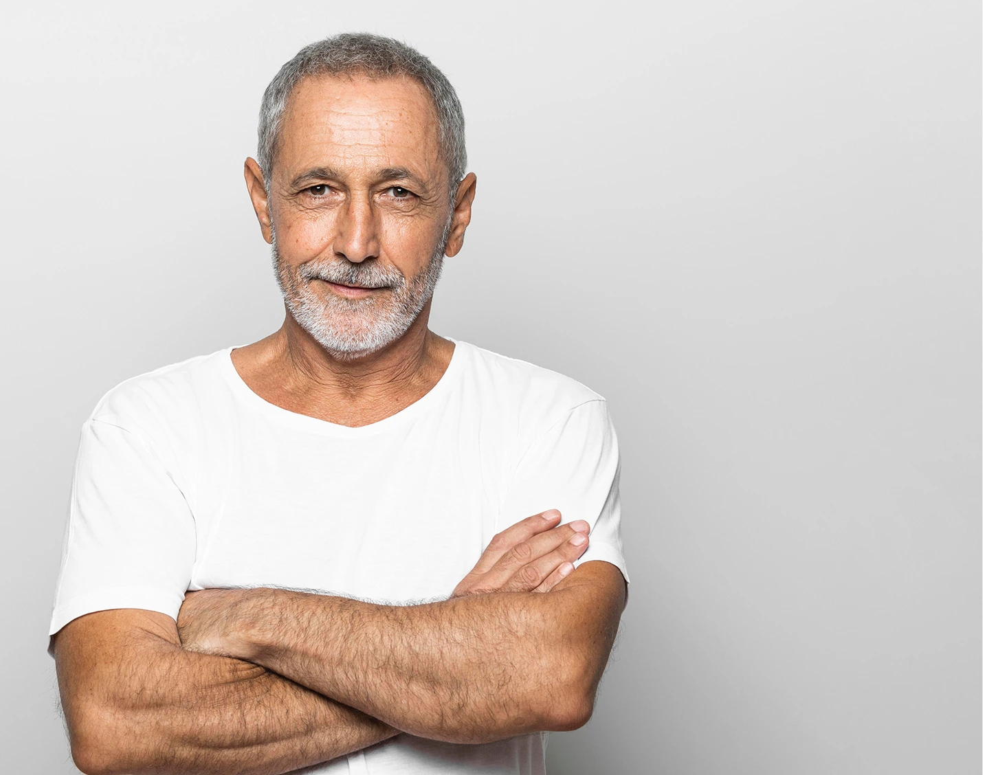 Older man with gray beard wearing white t-shirt with arms crossed