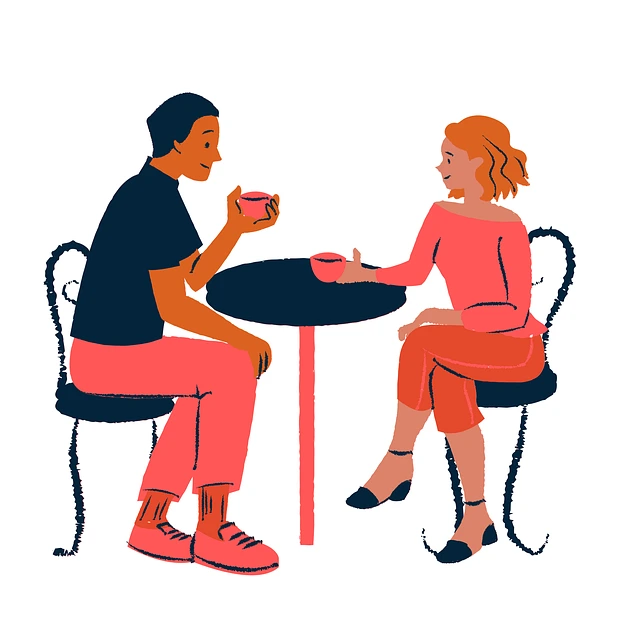 Two people sitting facing each other at a small table, each holding a cup, smiling in conversation