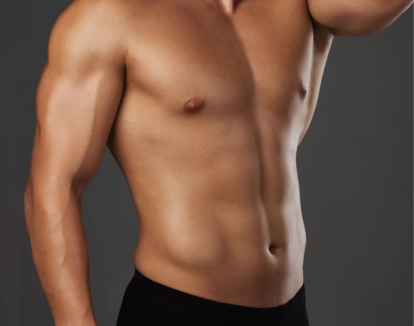 Shirtless man with defined abs and toned arms against gray background