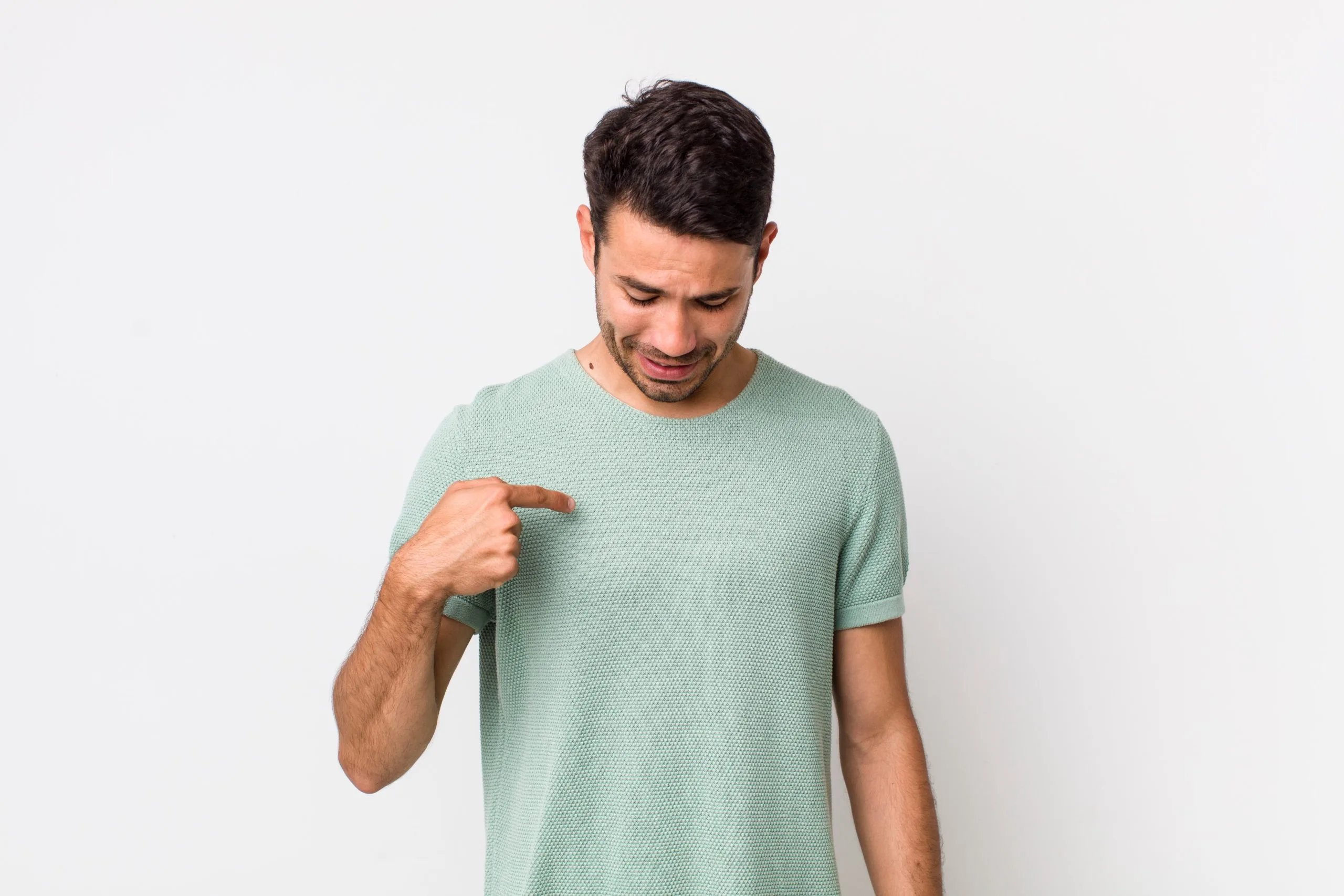 Man in light green shirt smiling and pointing to his chest area