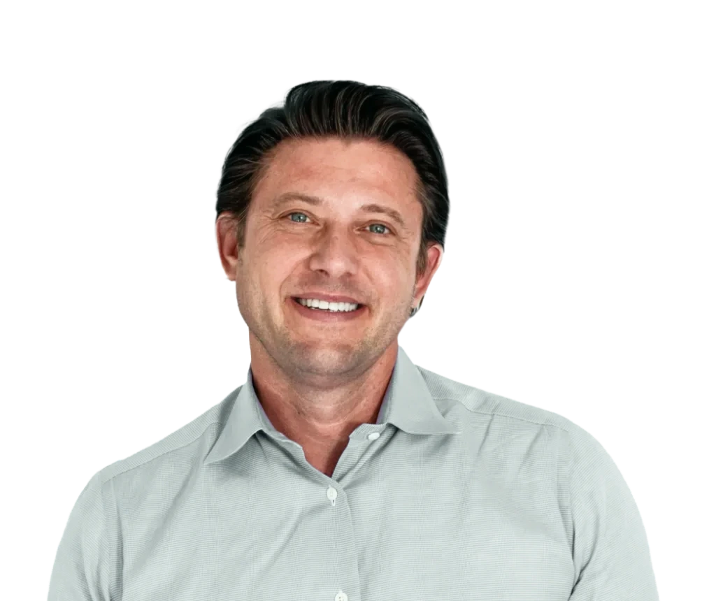 Man with dark hair smiling at camera, wearing light gray button-up shirt