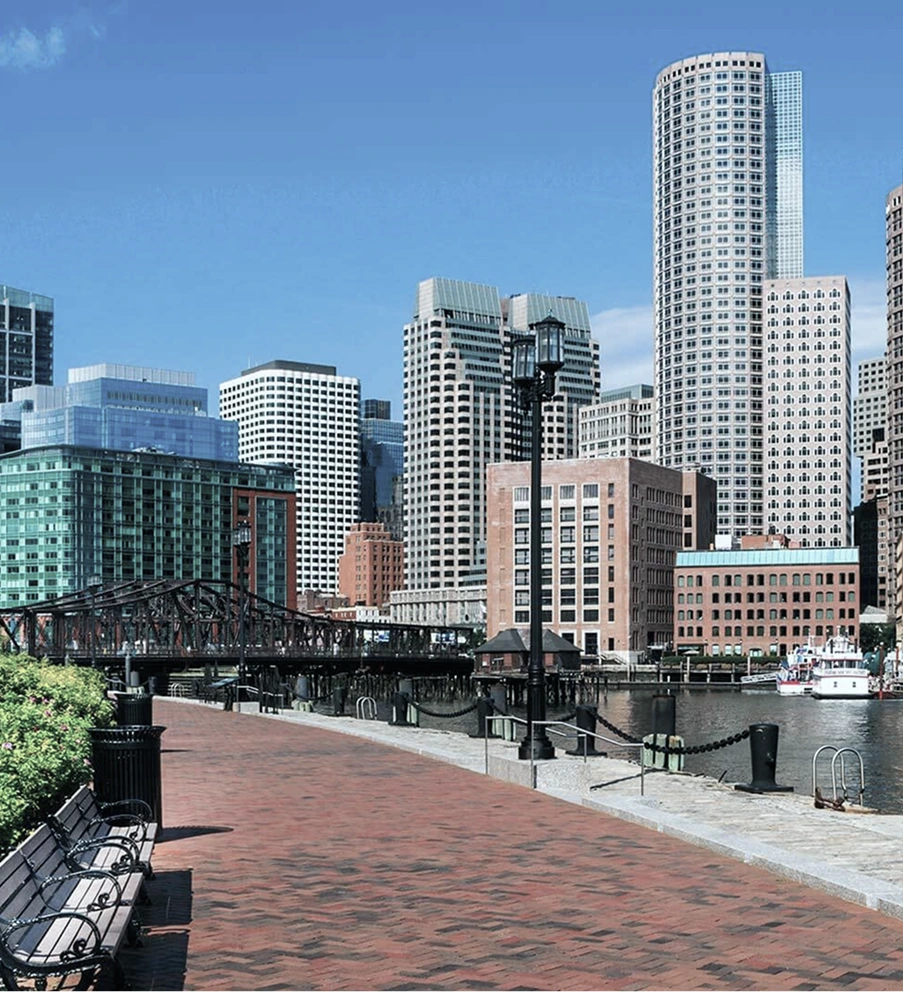 Urban waterfront with brick promenade, pedestrian bridge, and downtown skyscrapers along the water
