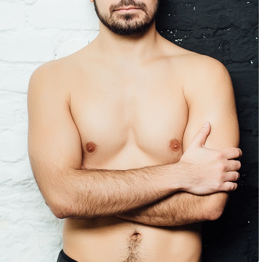 Shirtless man with beard standing against white and black wall with arms crossed