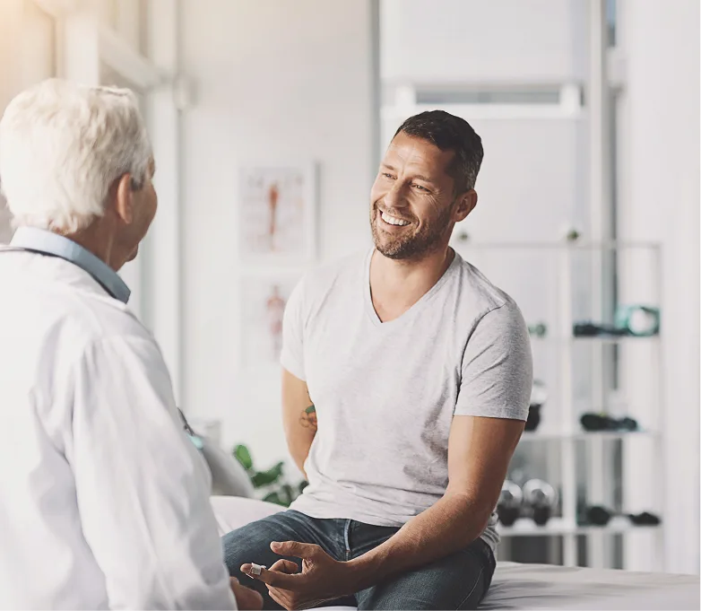 Smiling man in gray t-shirt speaking with older doctor in white coat in clinic