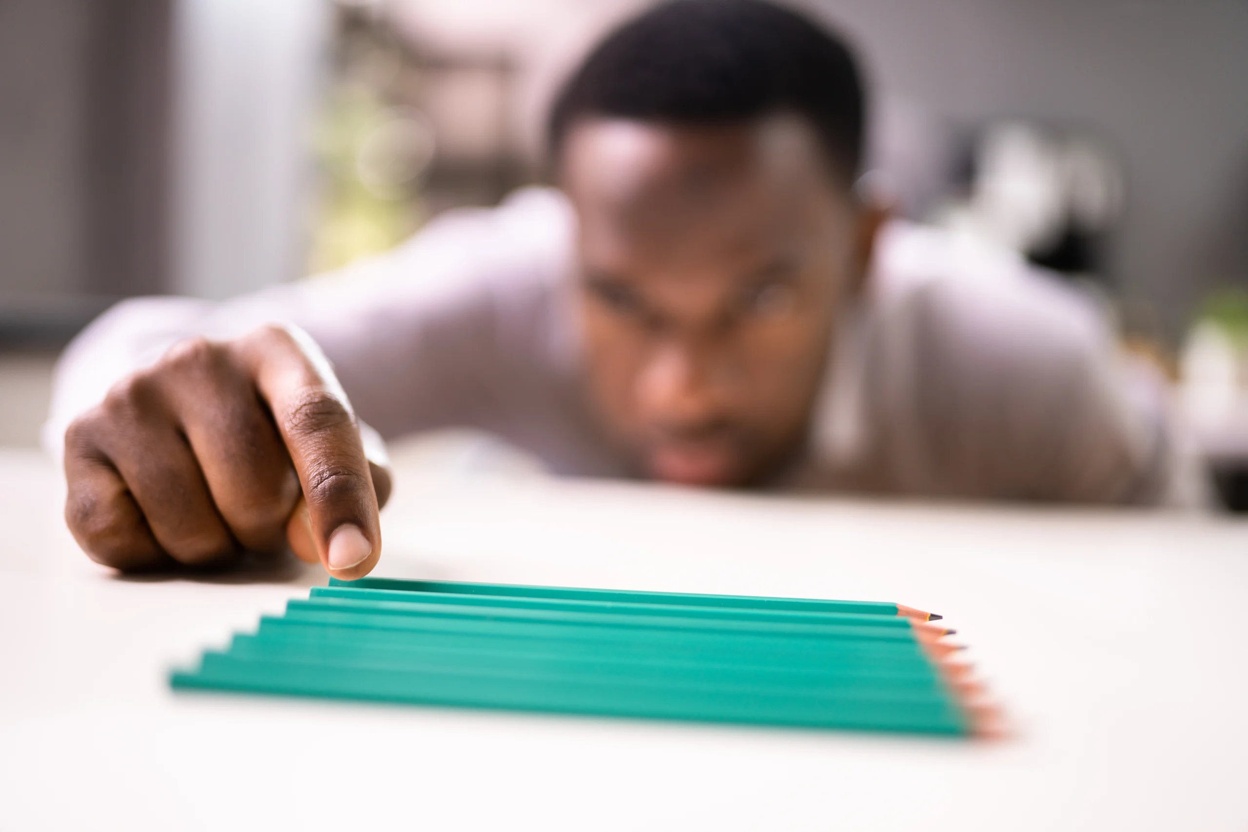 African American man carefully lining up a row of pencils on a table