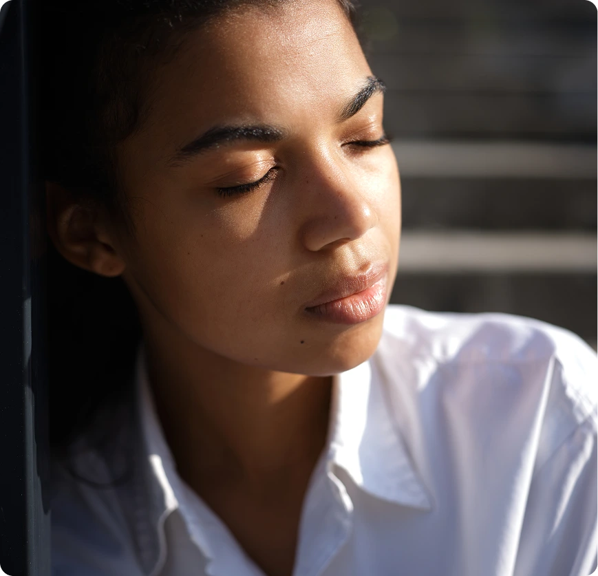 Person in thoughtful repose, eyes closed, wearing white shirt in natural light