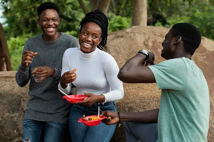 Three people smiling and eating outdoors in a natural setting