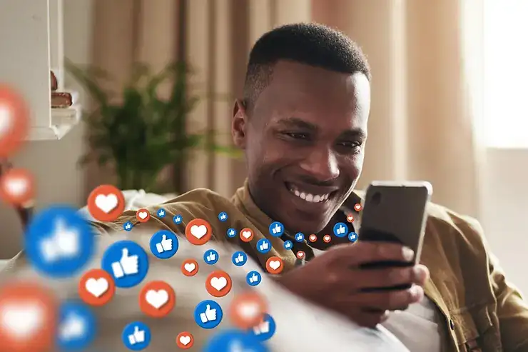 Man smiling while viewing smartphone with social media icons (hearts and thumbs-up) floating from screen