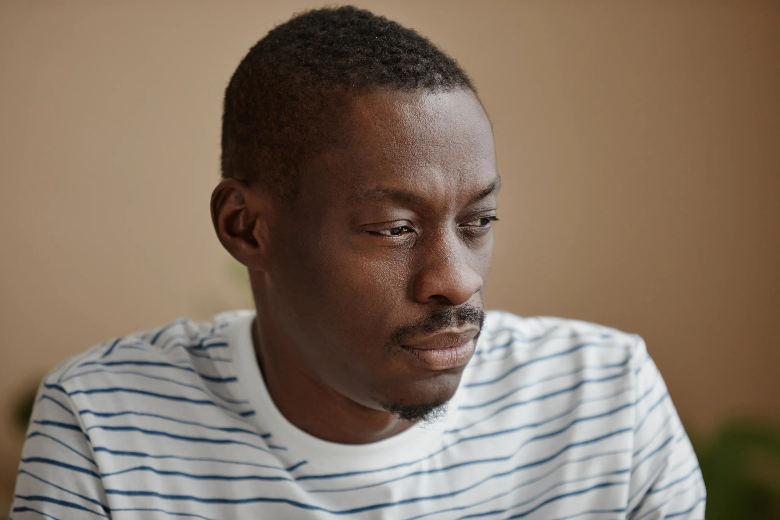 African American man in a striped shirt looking down thoughtfully