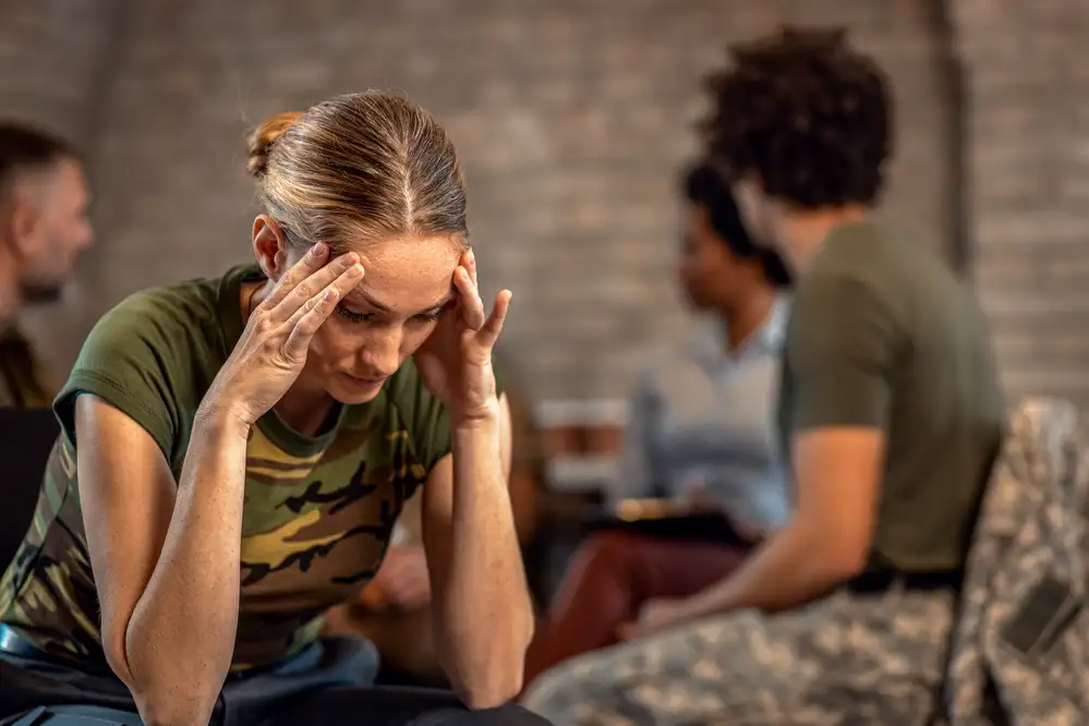 Woman in support group holding her head with both hands while sitting among other participants