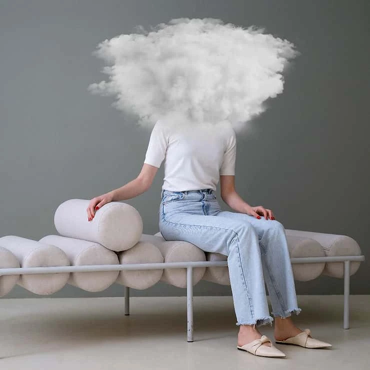 Person sitting on a bench with their head replaced by a large white cloud, symbolizing mental fog or anxious thoughts