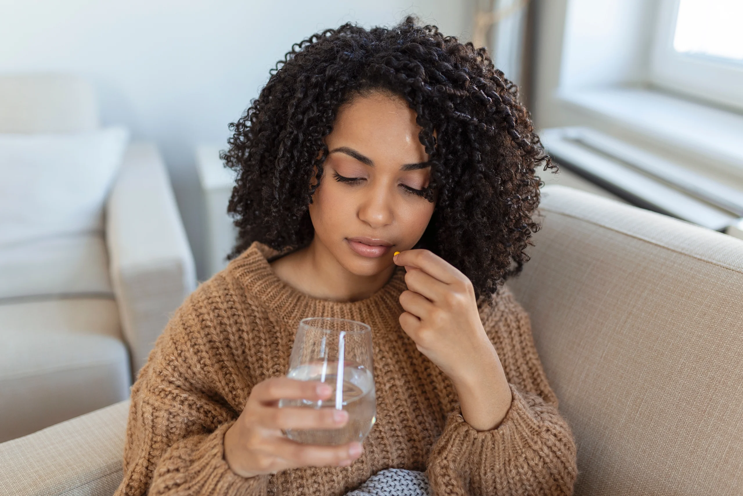 African American woman taking a pill with a glass of water at home