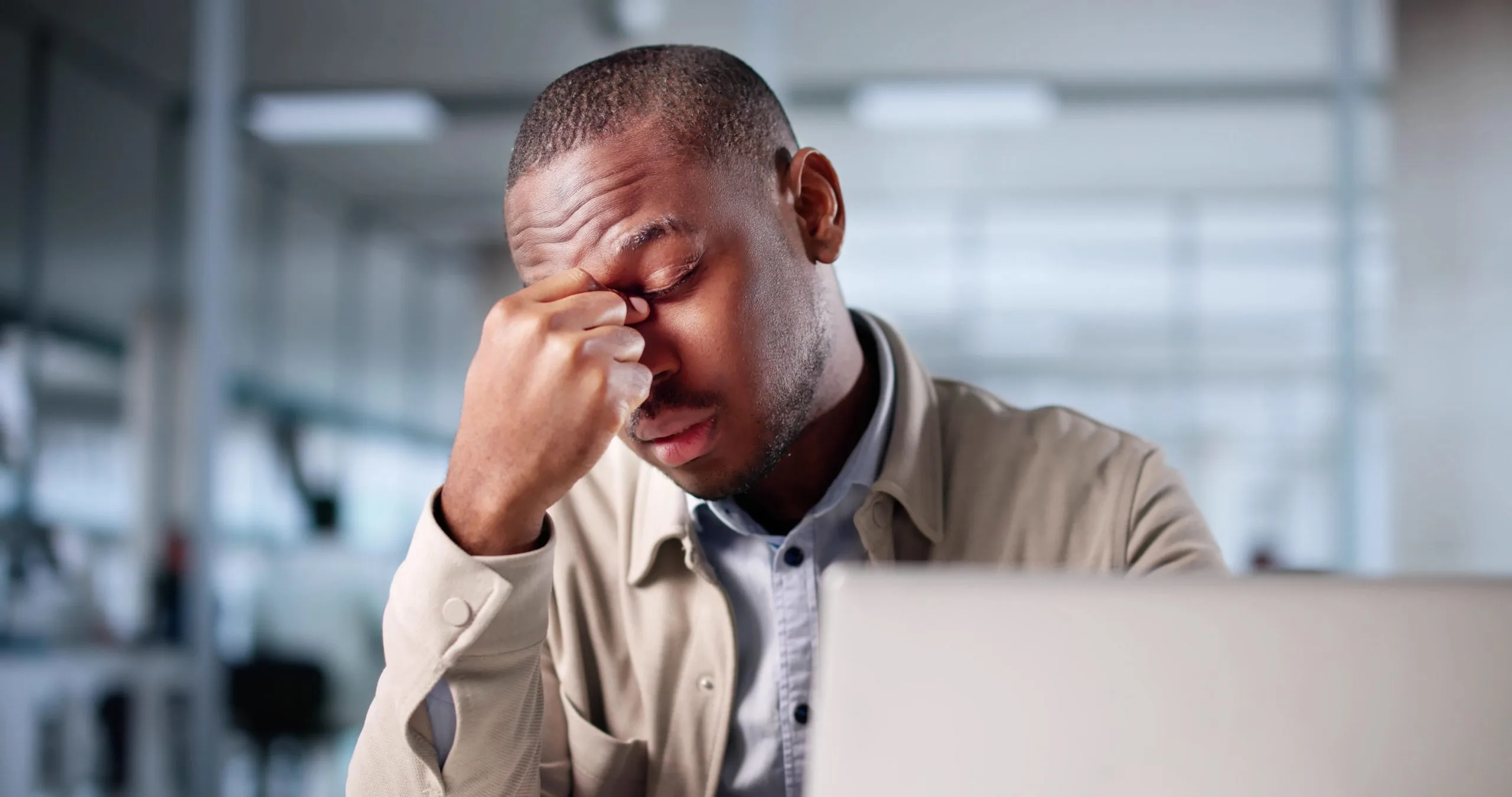 Stressed African American man rubbing the bridge of his nose at his laptop