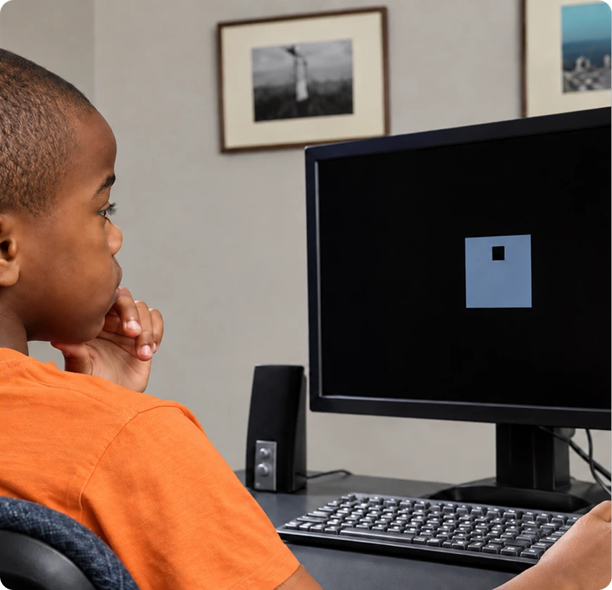 Child in orange shirt seated at desk, focused on computer monitor displaying a visual test pattern in a clinical office