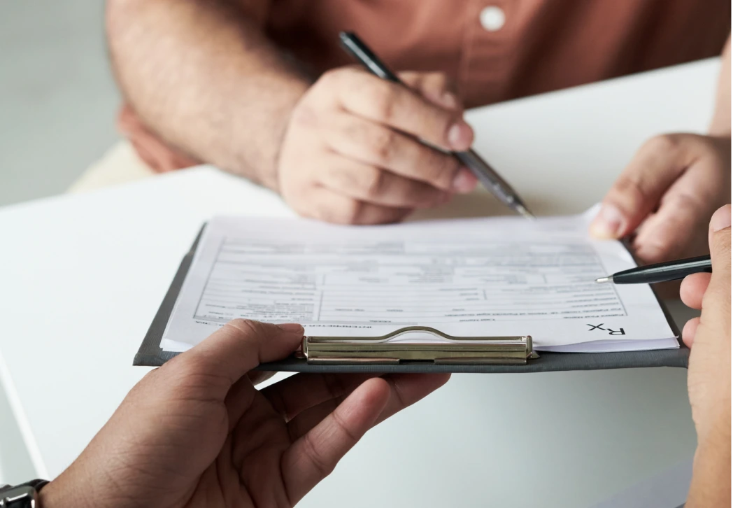 Person holding a clipboard with a medical form while another person fills it out with a pen