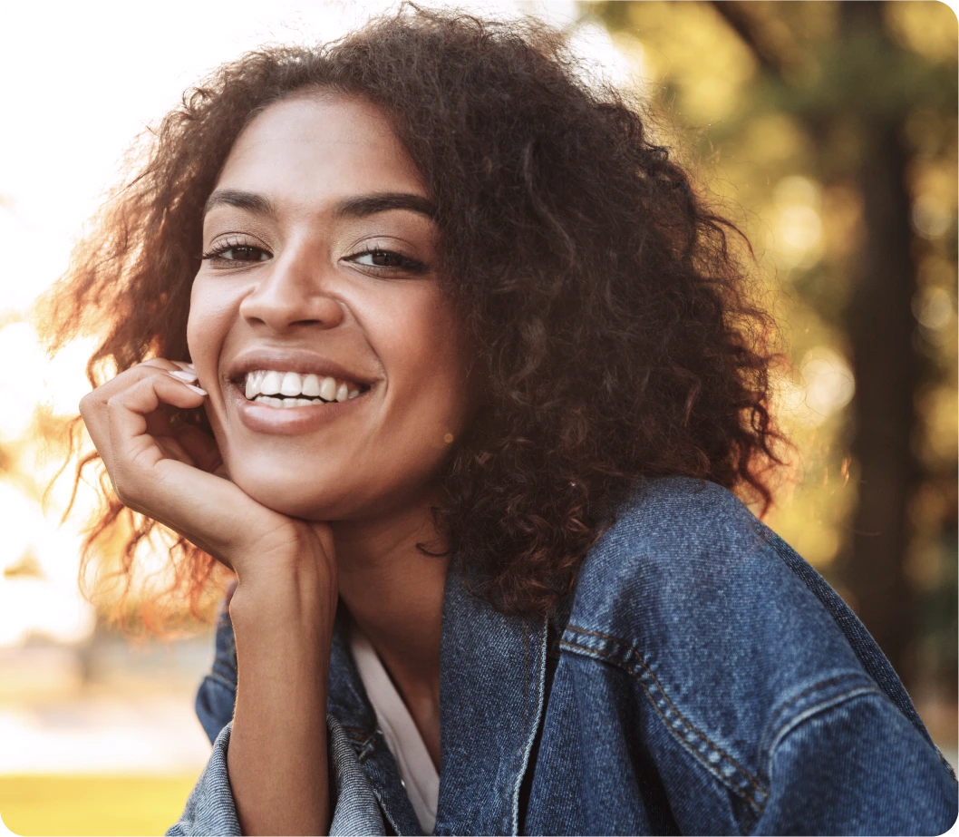 Woman smiling outdoors in natural sunlight, representing holistic wellness and mental health care