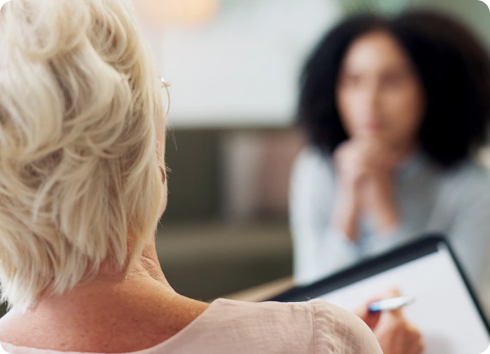 Older patient with white hair speaking with a healthcare provider holding a tablet during a consultation
